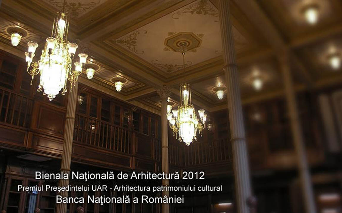 Sală înaltă din Palatul Băncii Naționale, cu galerii de lemn pe două niveluri și candelabre cu pandelocuri de cristal suspendate între coloane