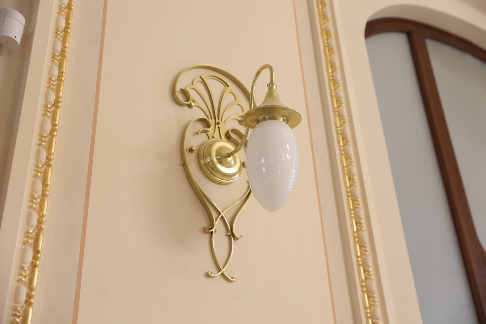 Aplică de perete Art Nouveau din alamă cu glob de sticlă opal, pe perete alb cu profile aurite