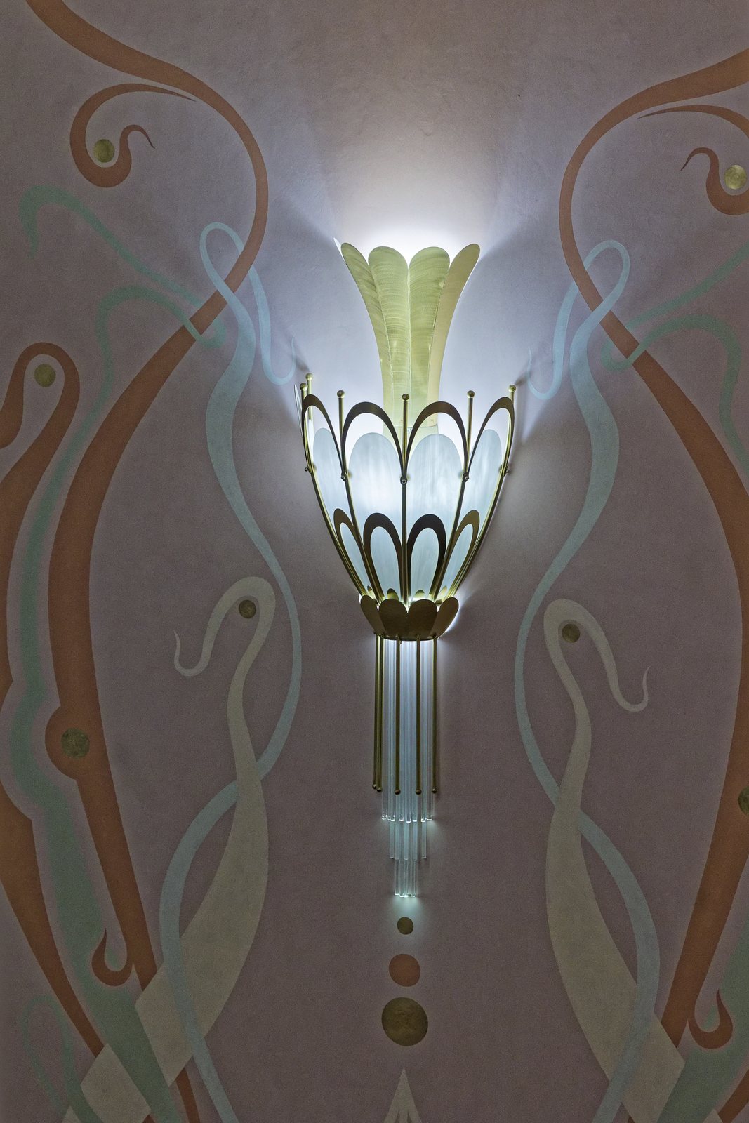 Aplică de perete Art Nouveau aprinsă, pe un perete cu decorație pictată în tonuri pastel
