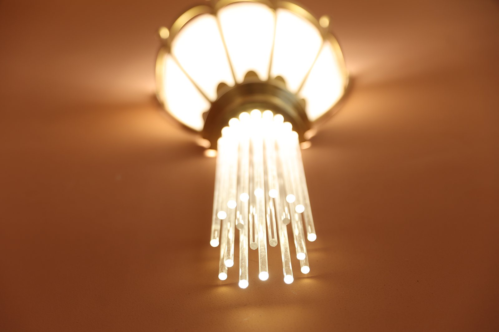 Detaliu al tijelor de sticlă luminate de sub o aplică de alamă