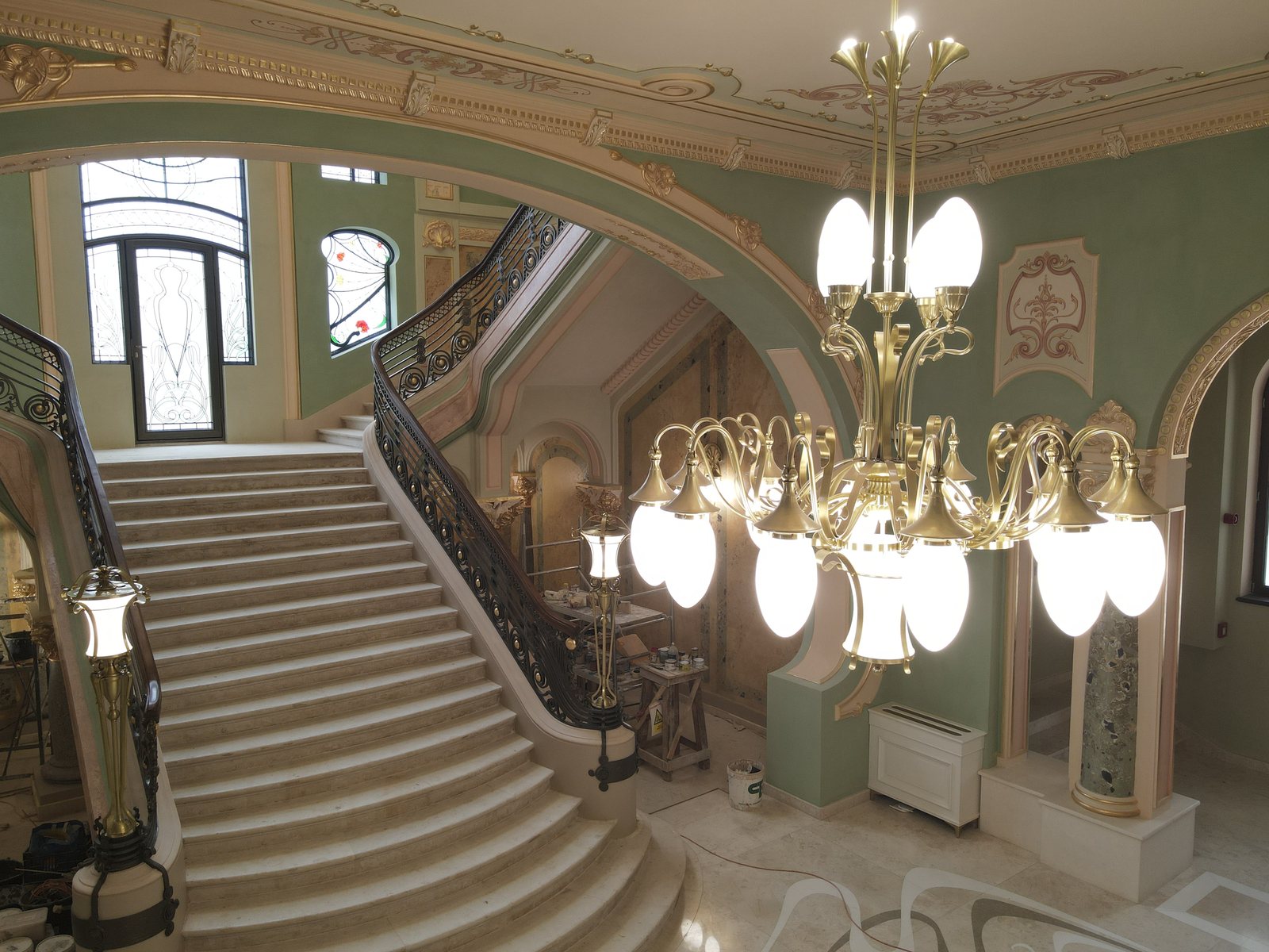 Candelabru de alamă cu brațe și globuri de sticlă, fotografiat de la nivelul lui, cu o scară de marmură în fundal