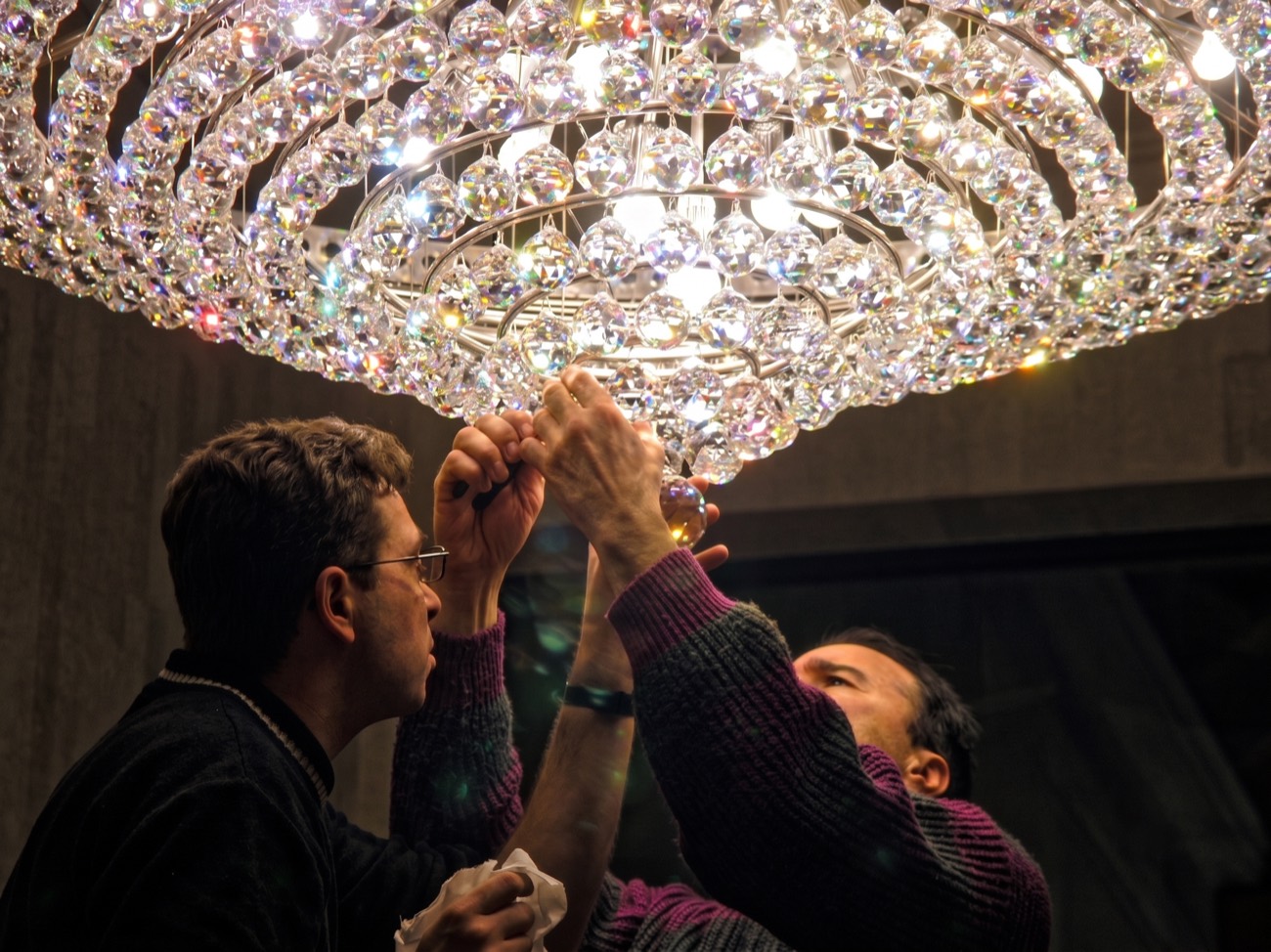 Doi meșteri montând sferele de cristal ale unui candelabru aprins