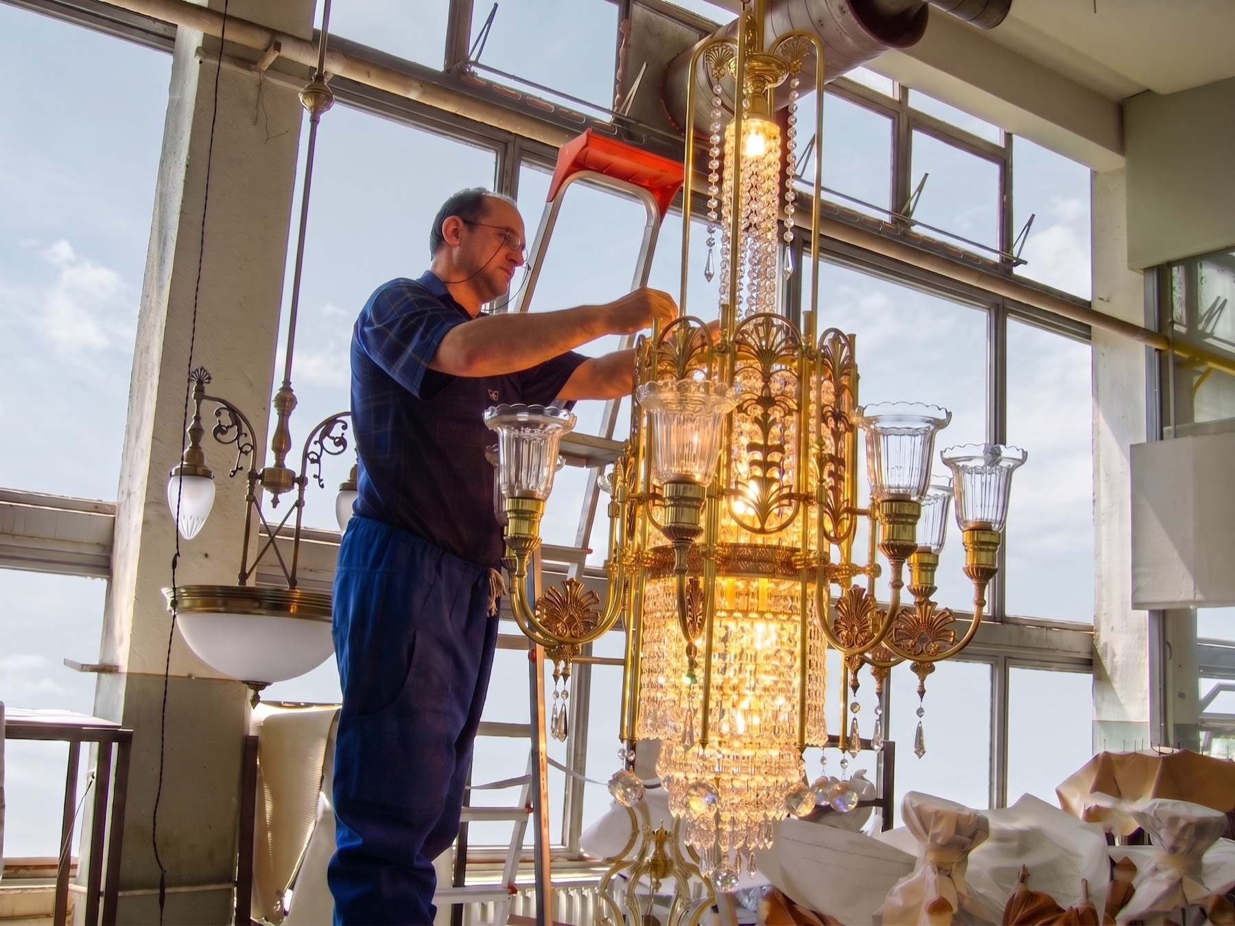 Meșter F.D. Stil finalizând un candelabru aurit cu cristale, în atelier