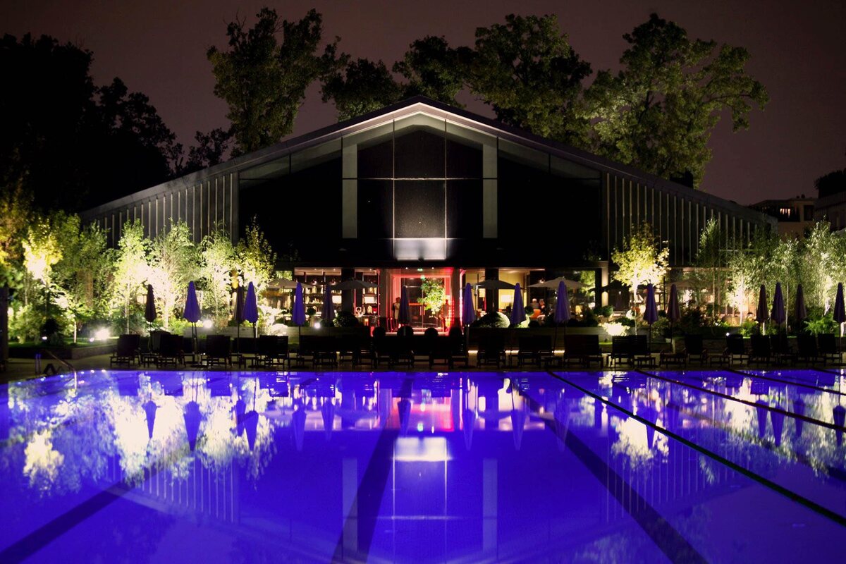 Piscina exterioară de la Stejarii Country Club noaptea, cu pavilionul restaurantului luminat în spate și copacii pădurii Băneasa de jur împrejur