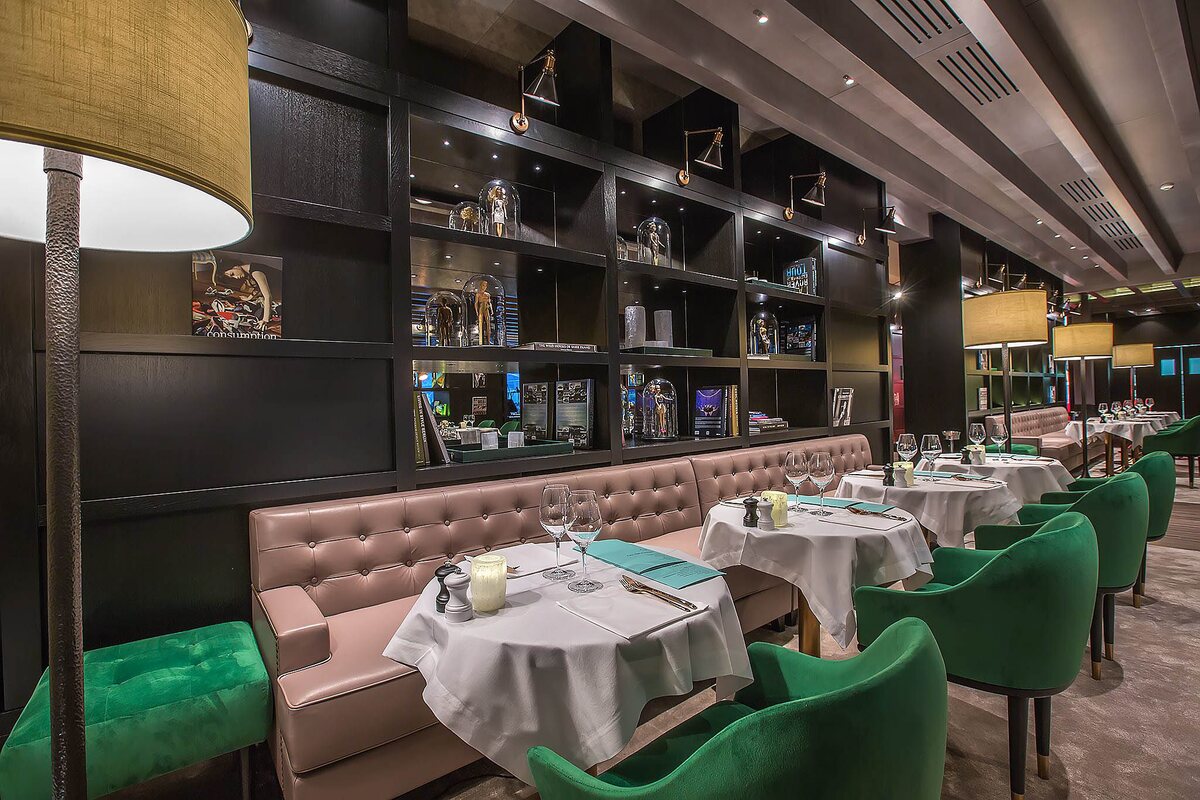 Sala restaurantului de la Stejarii Country Club: peretele-bibliotecă negru cu aplicele-reflector FD.STIL pe brațe de alamă și un lampadar cu abajur din alamă în prim-plan