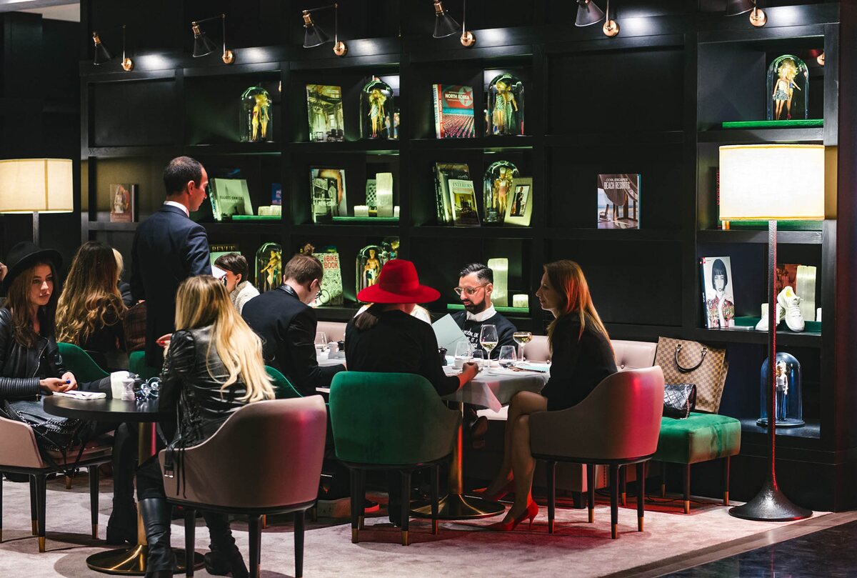 Restaurantul de la Stejarii Country Club plin de oaspeți seara, luminat de aplicele-reflector de pe bibliotecă și de lampadarele dintre mese